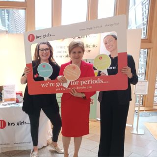 Nicola Sturgeon and hey girls staff in a hey girls photo frame next to a display stand with products